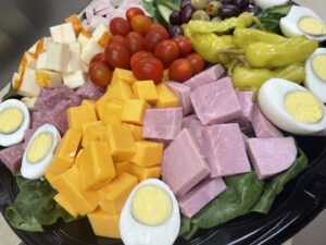 Party tray of ham, cheddar cheese, hard-boiled eggs, tomatoes, peppers, and black olives.